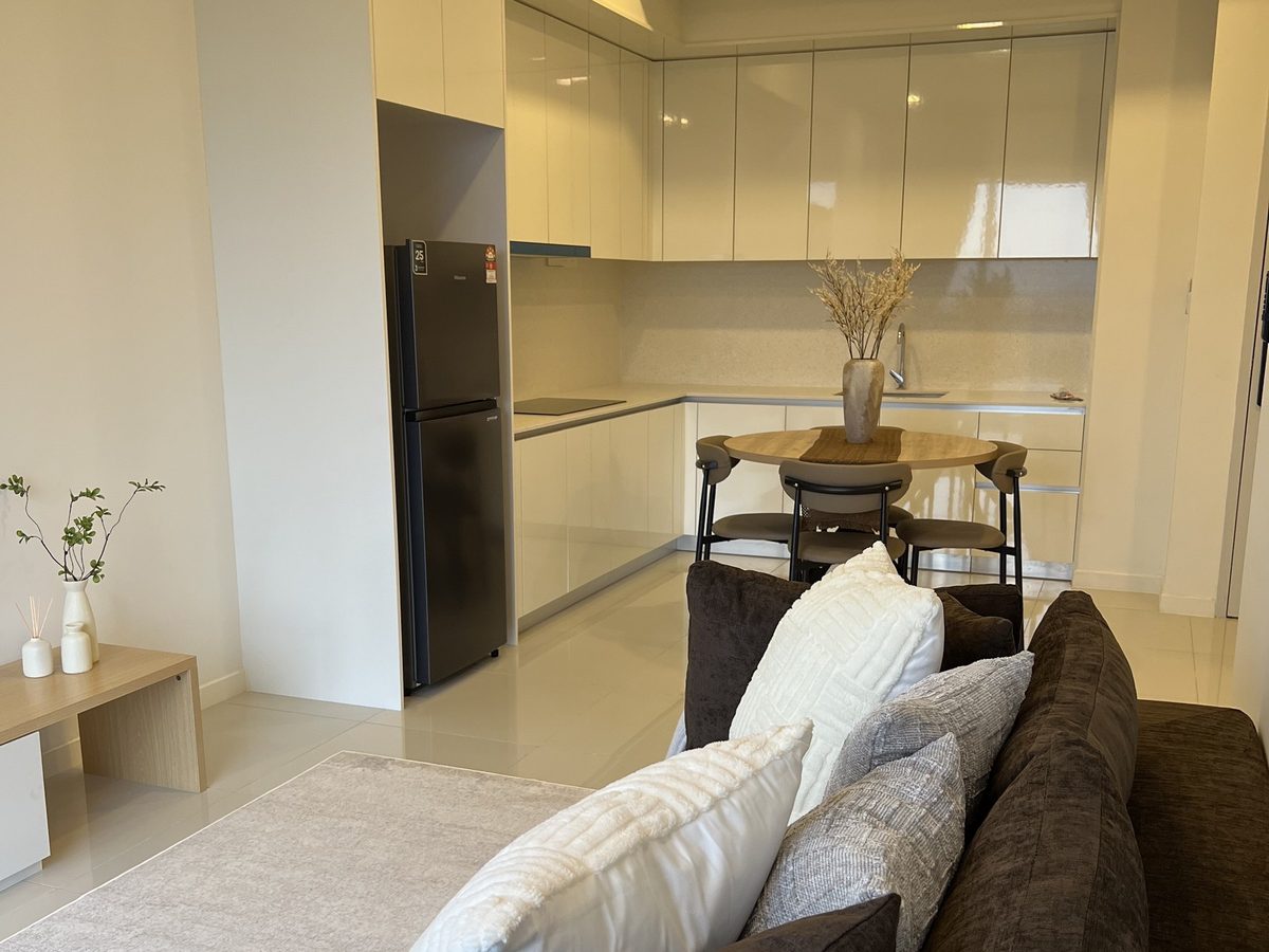 Dapur dengan kabinet krim dan peti sejuk, meja makan bulat kayu oak dan sofa di hadapan