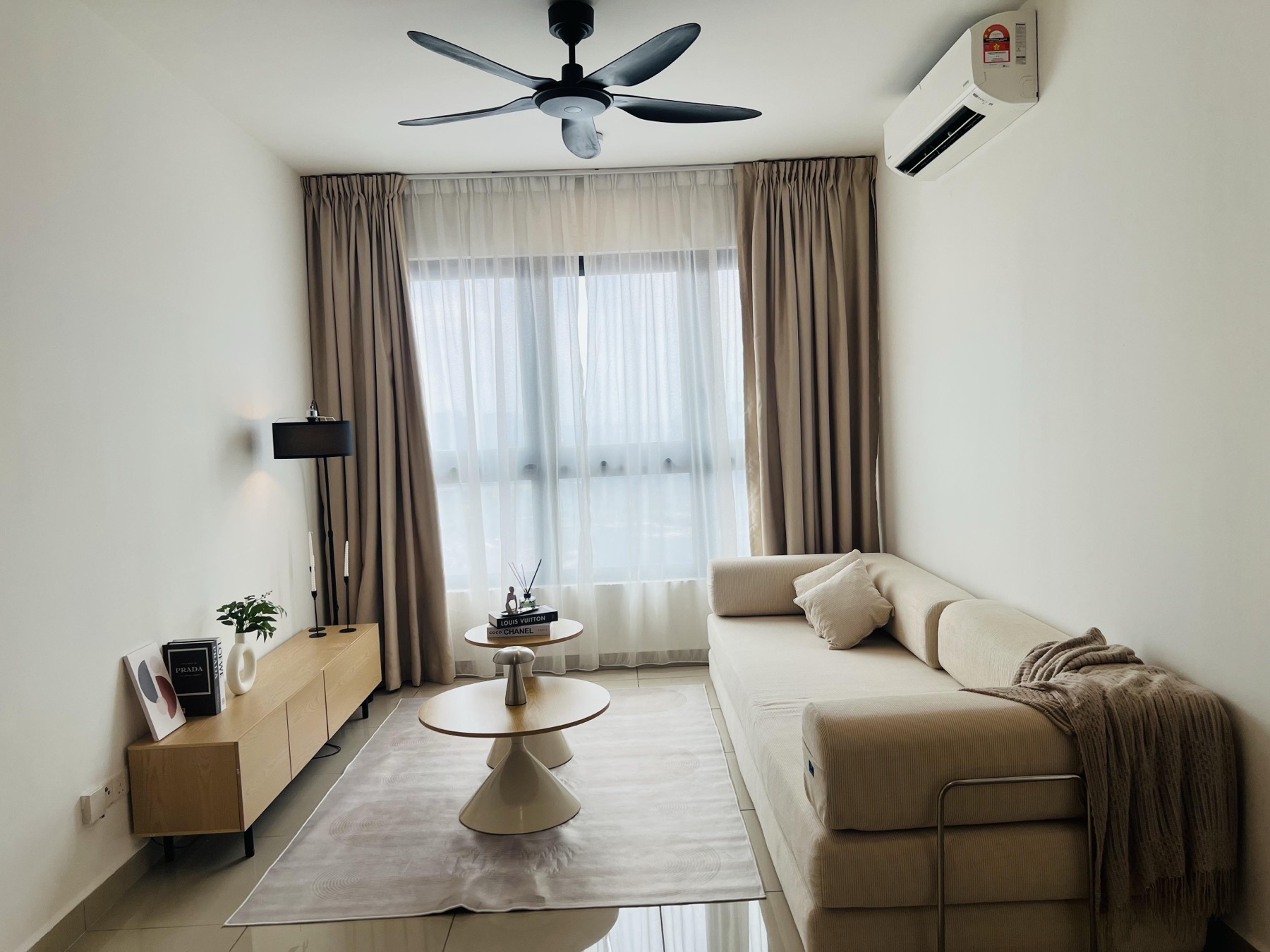 A furnished living room at M Vertica, Cheras — cream sofa, oak media console and layered curtains.